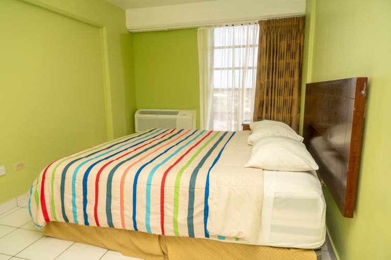 Bright lime green bedroom with a bed featuring colorful striped bedding, white pillows, wooden headboard, and a mounted TV on the wall