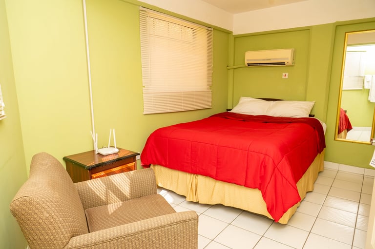 Bright green bedroom with a red-covered bed and beige armchair at BayPort Residence Inn