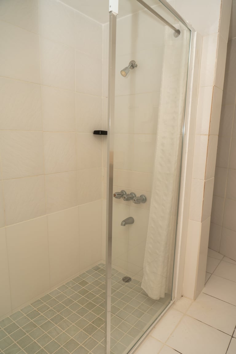 Modern glass shower enclosure with metal framing, clear glass doors, and tiled walls in a white bathroom
