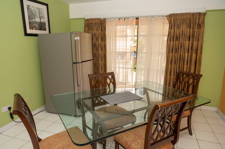 Modern dining room with glass table, wooden chairs, green walls, and stainless steel refrigerator