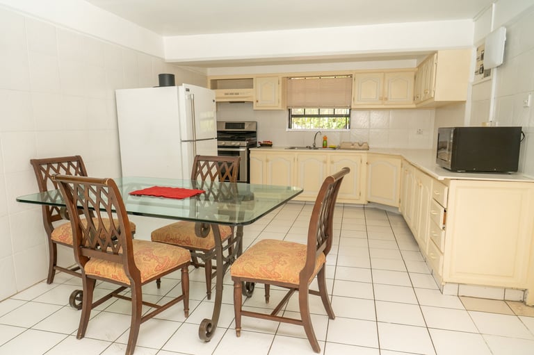 Kitchen dining area with glass table, wooden chairs with cushions, and light wood cabinetry along the walls