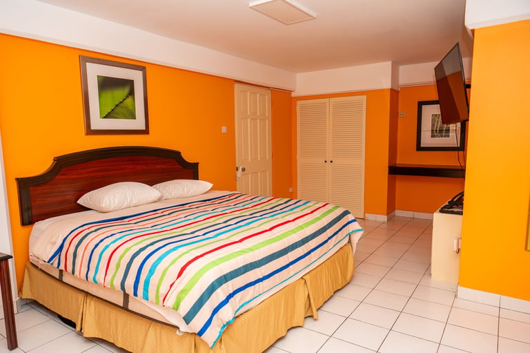 Bright orange bedroom with a wooden bed, colorful striped bedding, and tile flooring