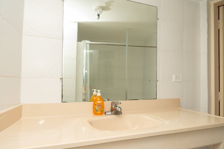 Modern bathroom vanity with cream countertop, single sink, large mirror, and glass shower enclosure in the background