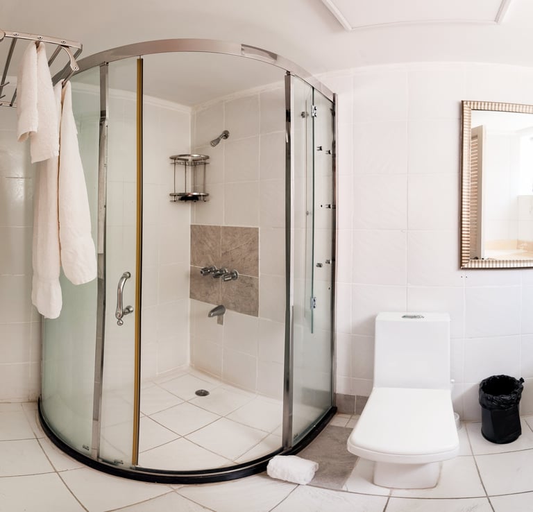 Modern bathroom with curved glass shower enclosure, white toilet, and white tile flooring