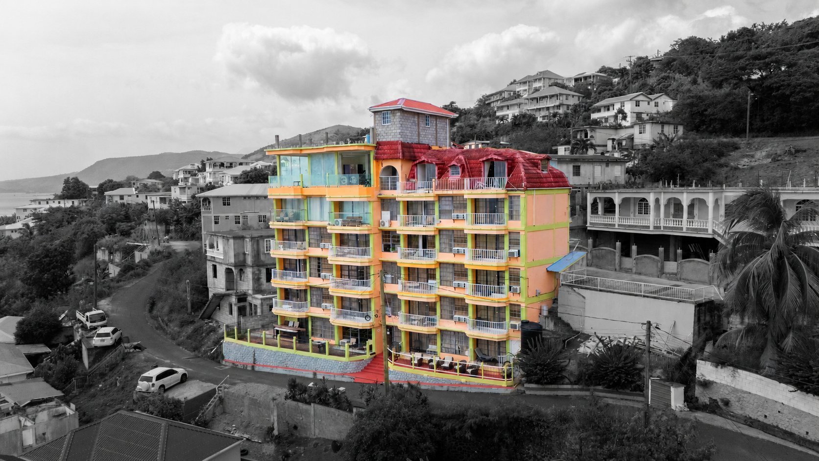 Colorful multi-story BayPort Residence Inn building with yellow, orange, and red facade on a hillside coastal town with the Caribbean Sea in the background
