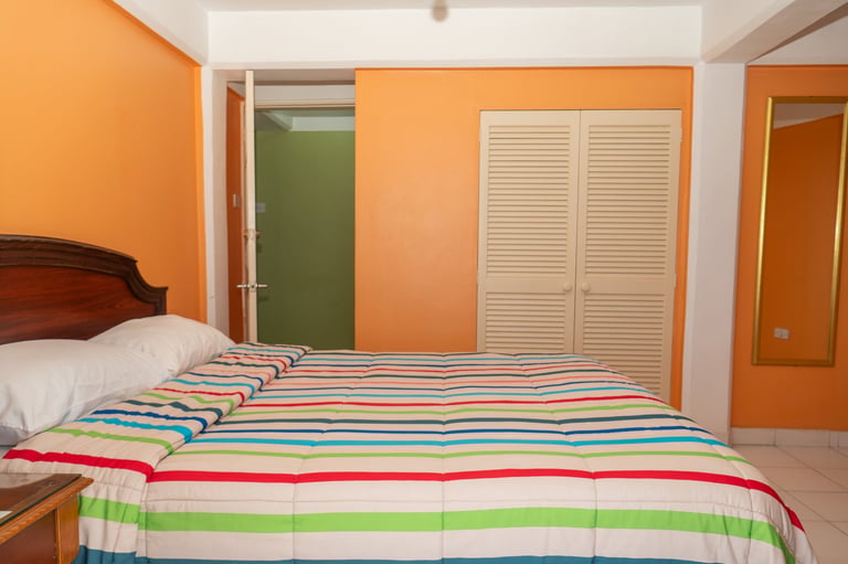 Bedroom with bright orange walls, wooden bed with colorful striped bedding, and white louvered closet doors