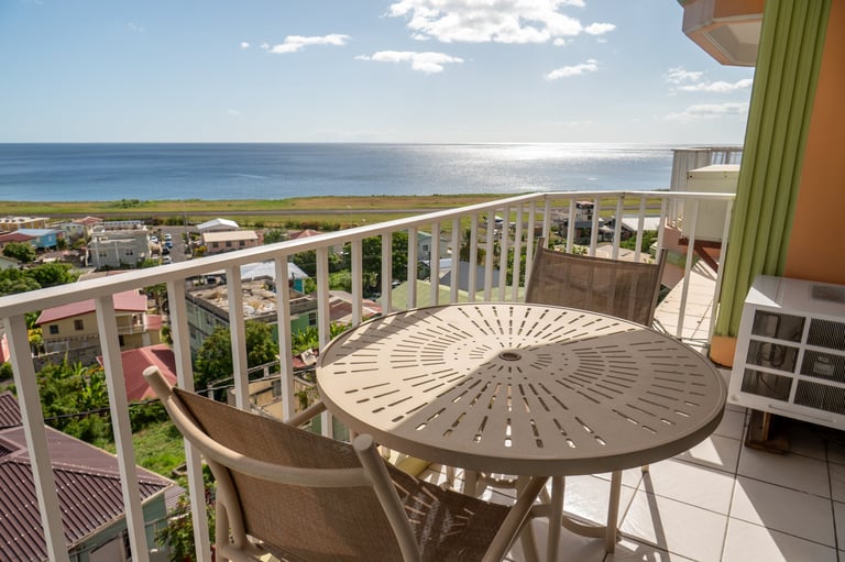 Elevated balcony with round table and chair overlooking ocean and coastal landscape