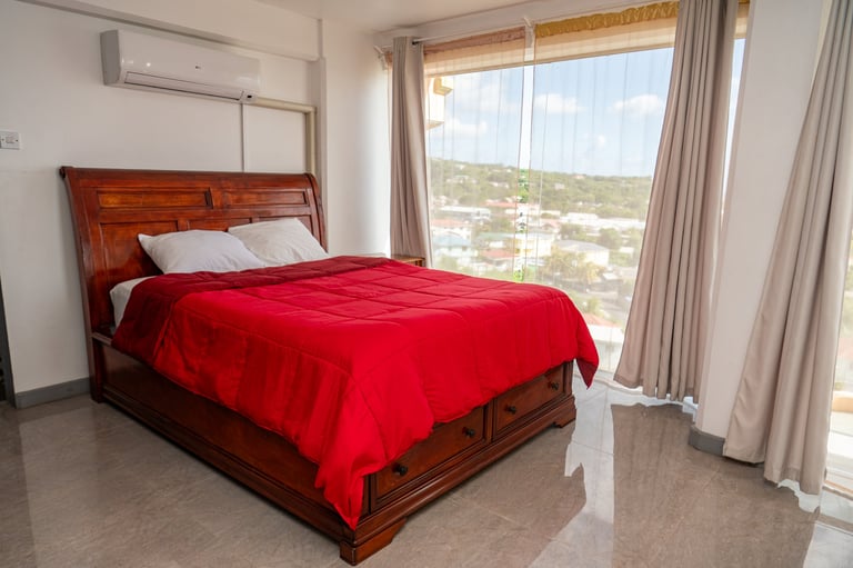 Modern bedroom with wooden bed, red bedding, and hillside views