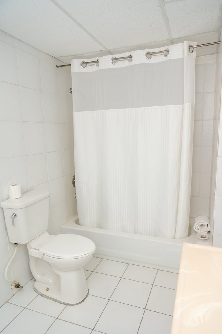 Clean white bathroom with toilet, bathtub, shower curtain, and tiled floor