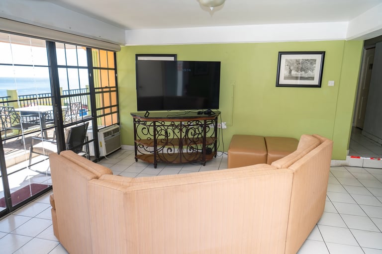 Bright living room with beige curved sofa, wall-mounted TV, lime green walls, and ocean view