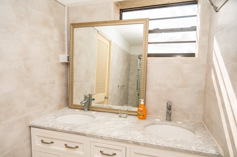 Bathroom vanity with marble countertop, gold-framed mirror, and cream-colored cabinet drawers below