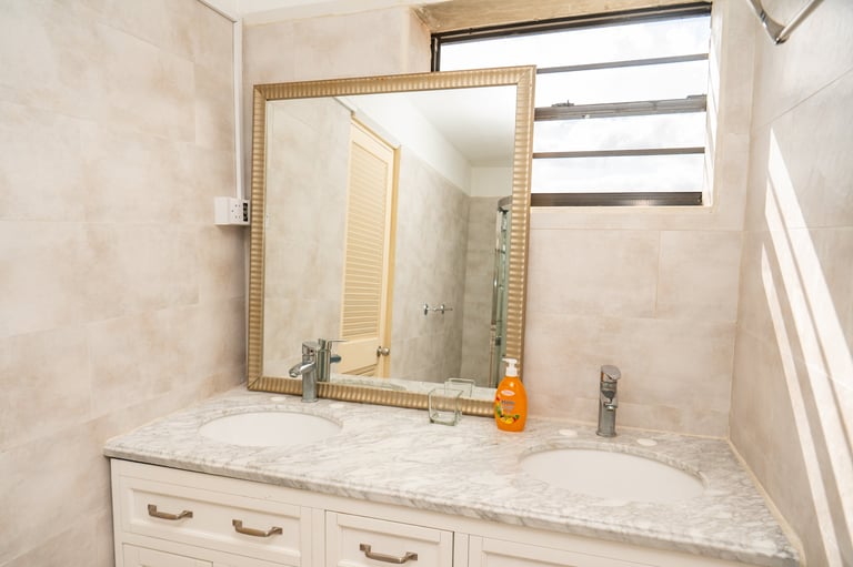 Bathroom vanity with marble countertop, gold-framed mirror, and cream-colored cabinet drawers below