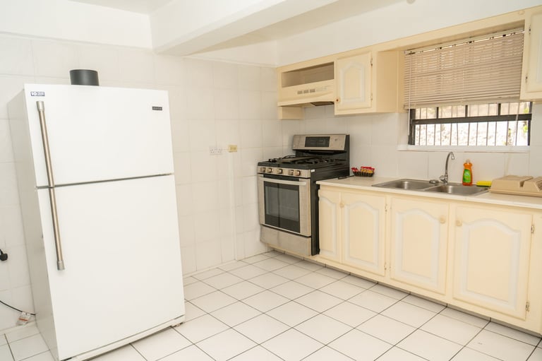 Small kitchen with white refrigerator, gas stove, beige cabinets, and tile flooring