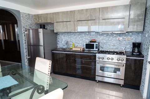 Modern kitchen with stainless steel appliances, light wood cabinets, blue tile backsplash, and dark lower cabinets