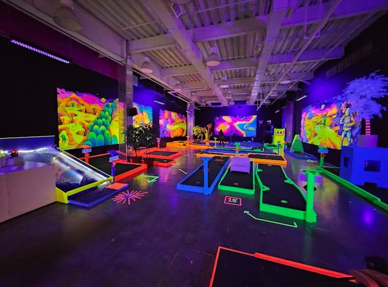 Interactive neon art gallery with glowing digital displays, colorful projections, and illuminated floor installations under purple ambient lighting