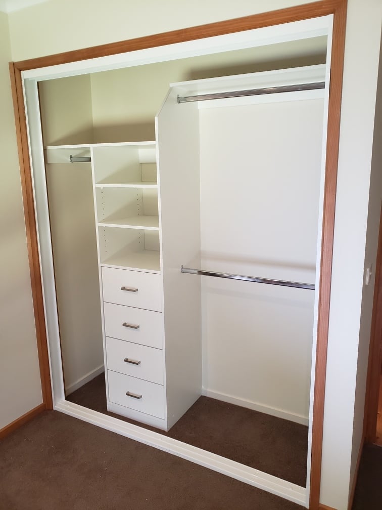 Custom built-in wardrobe with white shelving, drawers, and hanging rods on carpeted floor