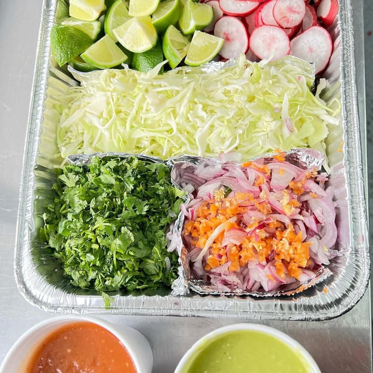 Overhead view of a prepared salad kit with lime wedges, radishes, shredded cabbage, greens, and pink pickled onions