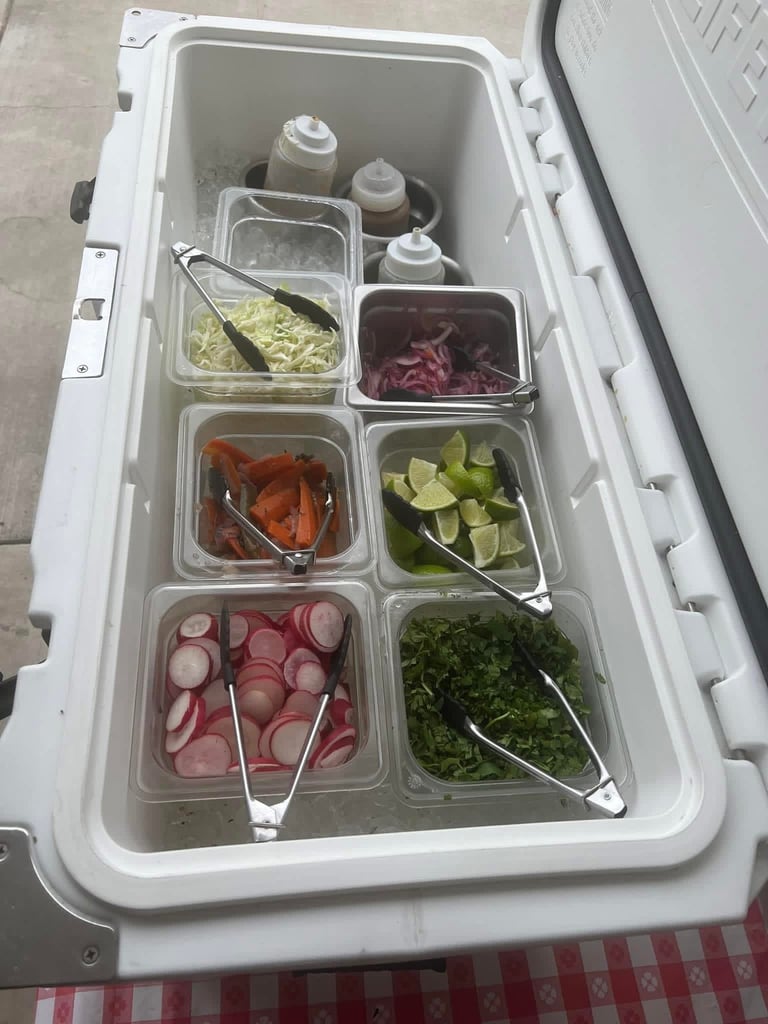 White cooler filled with clear containers of fresh vegetables including lettuce, radishes, peppers, cucumbers, and herbs