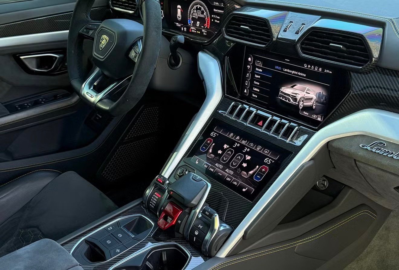 Luxury sports car interior with leather steering wheel, digital dashboard, multiple screens, and center console with gear shift