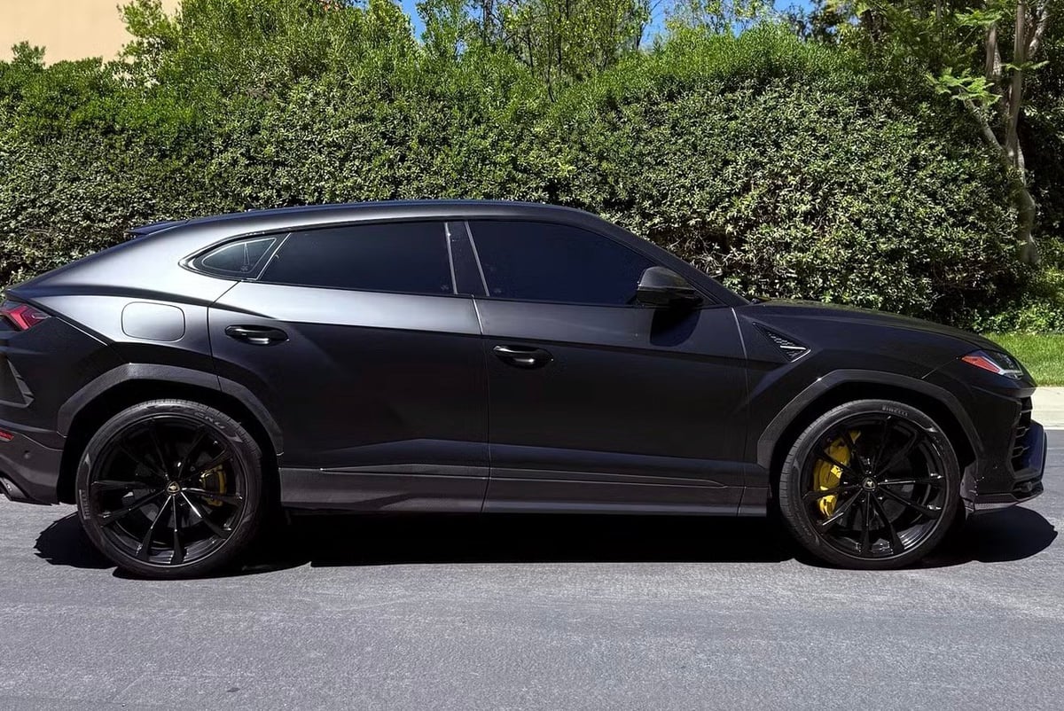 Black luxury sports SUV with dark wheels parked in front of green hedge backdrop