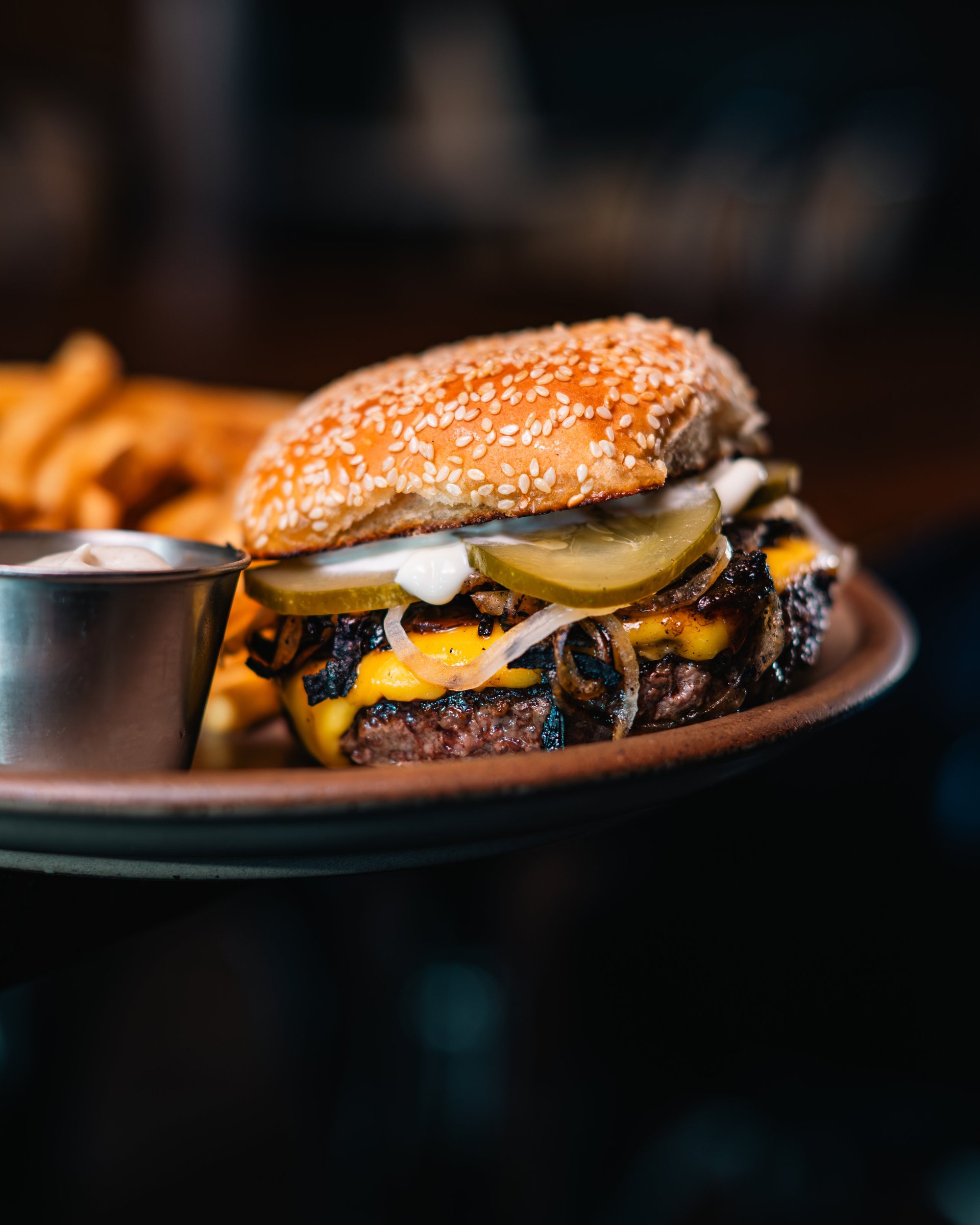 Gourmet burger with sesame bun, melted cheese, caramelized onions, and pickles served on a plate with fries