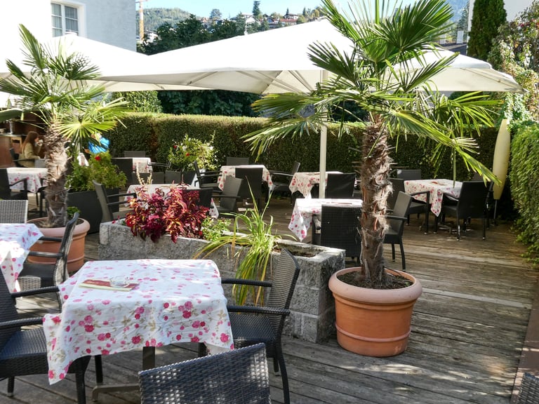 Terrasse mit gedeckten Tischen, Palmen und Sonnenschirmen auf hölzernem Boden im Sommerschatten