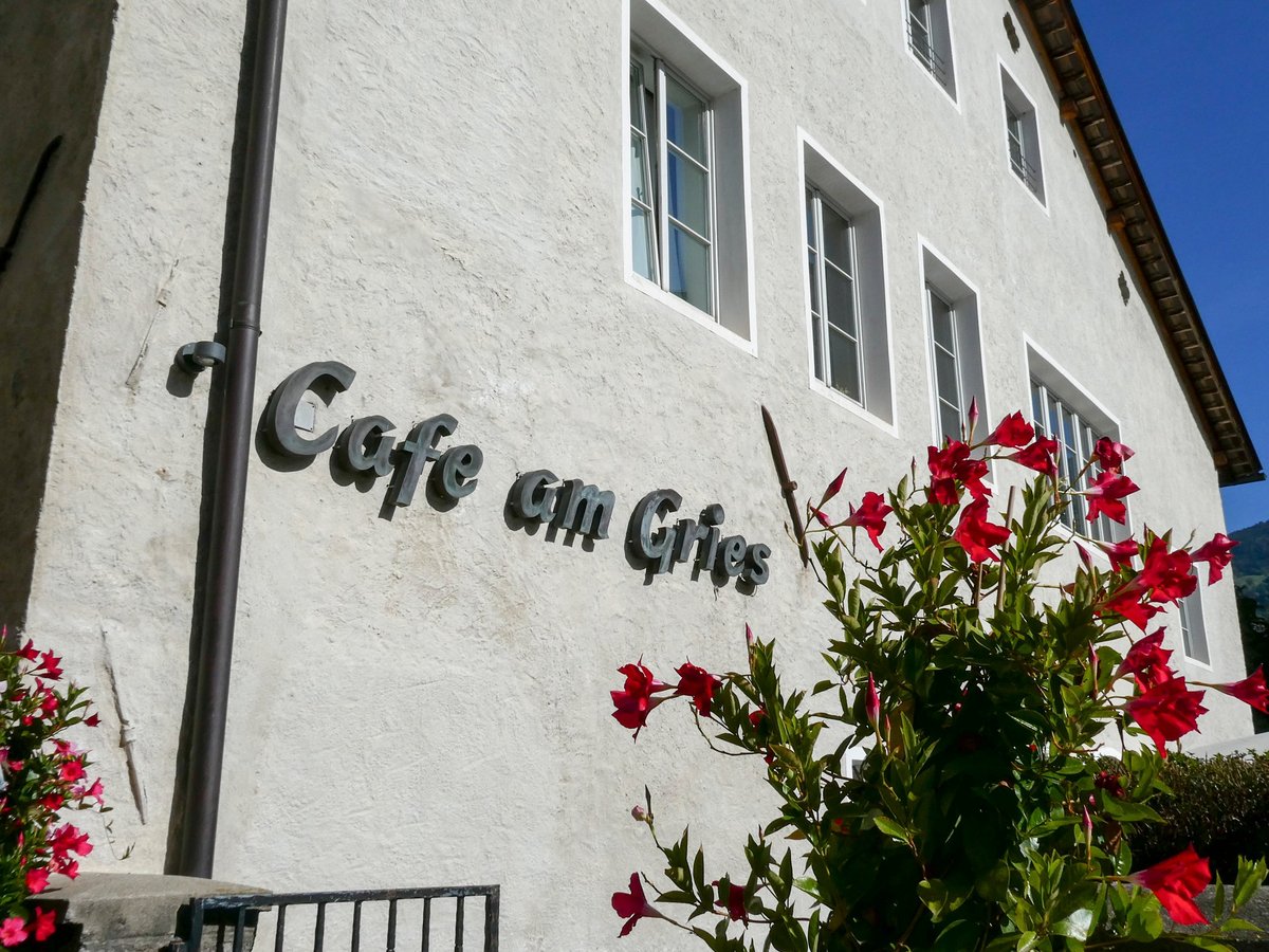 Weiß getünchtes Gebäude des Café am Gries mit Schriftzug an der Fassade und blühenden roten Blumen davor