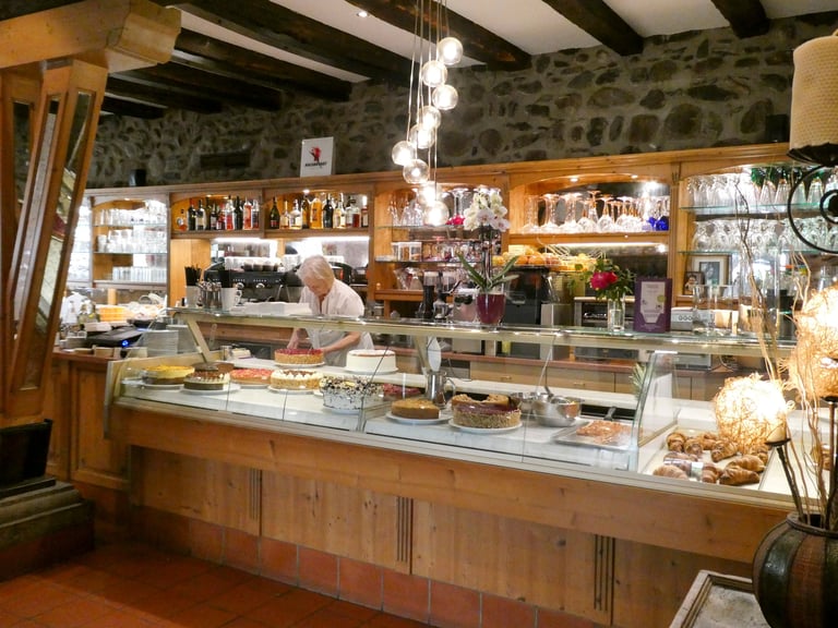 Blick über die Bar des Café am Gries mit Vitrine voller Torten und Kuchen, Holzvertäfelung und historischem Mauerwerk