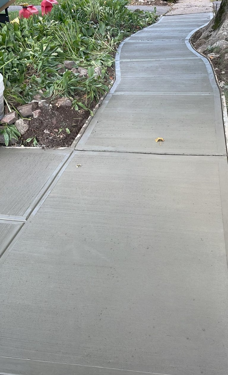 Curved concrete walkway running alongside a garden bed with pink flowers and green plants
