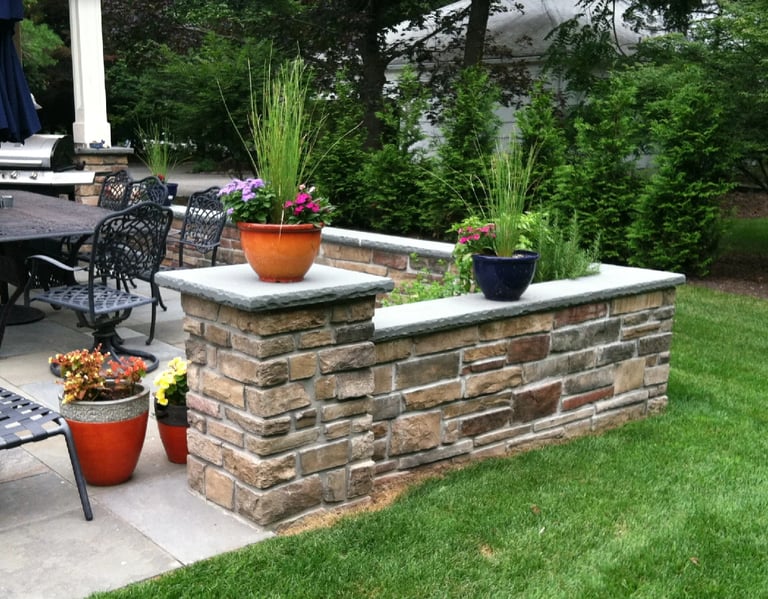 Brick planter boxes with colorful potted flowers on a patio, surrounded by lawn and patio furniture
