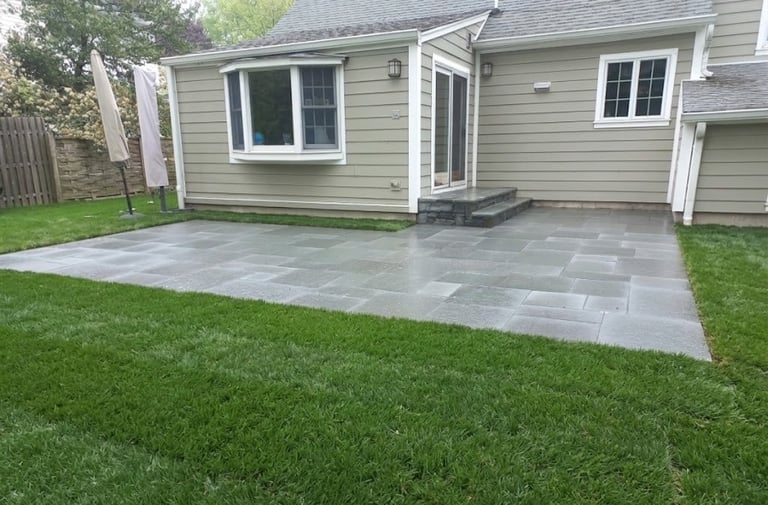 Modern house with gray stone patio, green lawn, white trim, and large windows in residential backyard setting
