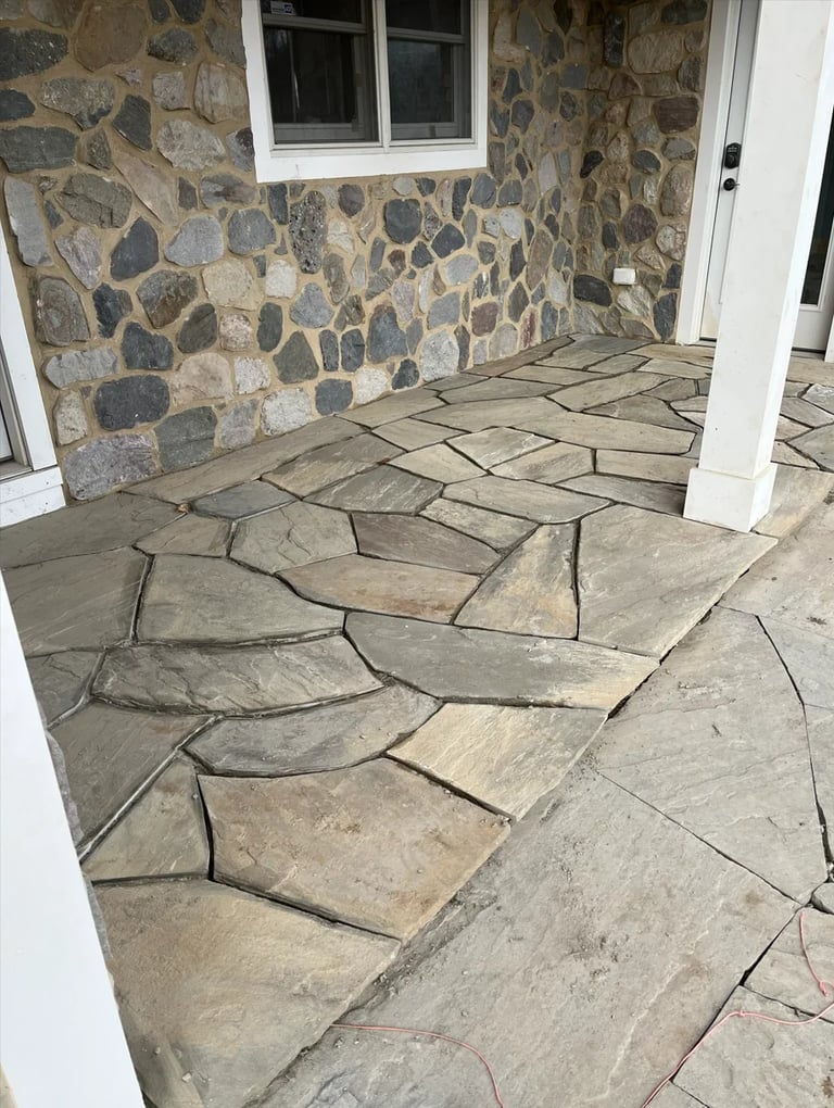 Outdoor patio with irregular flagstone flooring and stone wall under a white-framed window