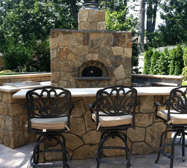 Stone outdoor pizza oven with bar seating featuring cast iron chairs with cushions on a patio