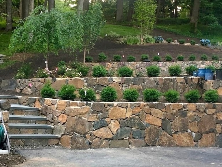 Tiered stone retaining walls with planted landscaping and trees in a woodland garden setting