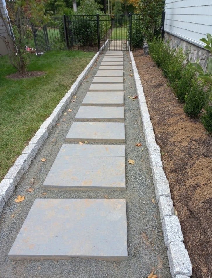 Concrete stepping stone pathway lined with gravel and hedges leading to a gate in a residential yard