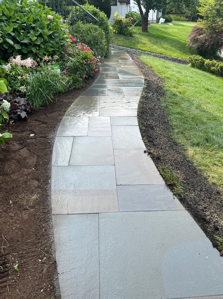 Stone paver pathway curving through a manicured garden with flowering plants and green lawn on both sides