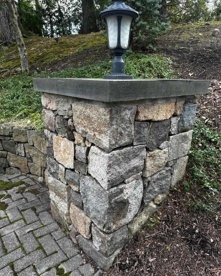 Stone pillar post with black lamp mounted on top in a garden setting surrounded by moss and trees