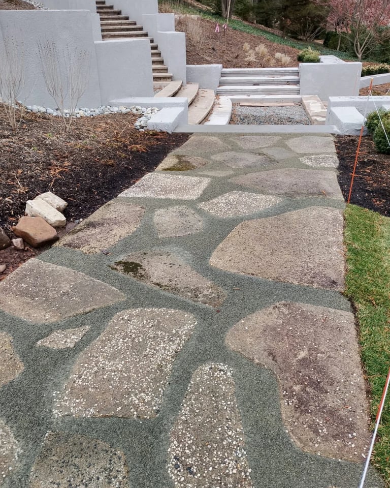 Modern landscape with decorative concrete pathway featuring organic shapes, white stepped retaining walls, and mulched garden beds on a hillside