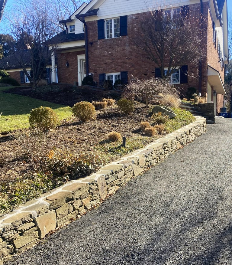 Two-story brick house with stone retaining wall and landscaped front yard with ornamental grasses and bare trees