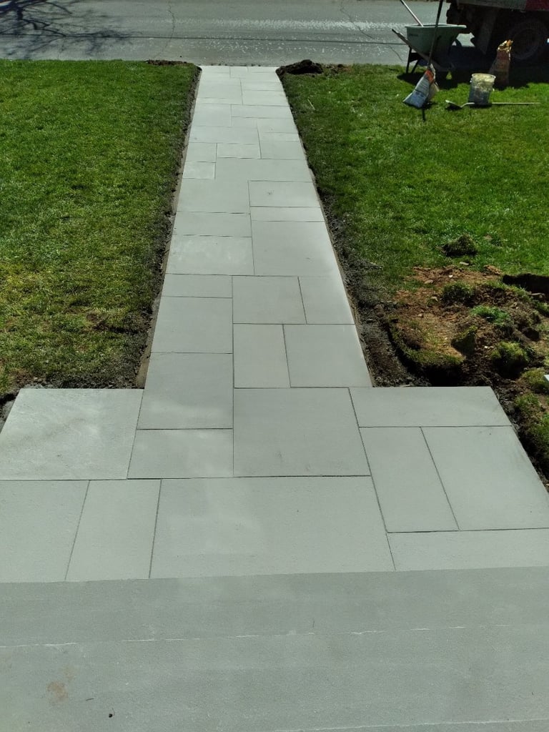 Concrete stone pathway with staggered rectangular pattern running through green lawn with landscapers working in background