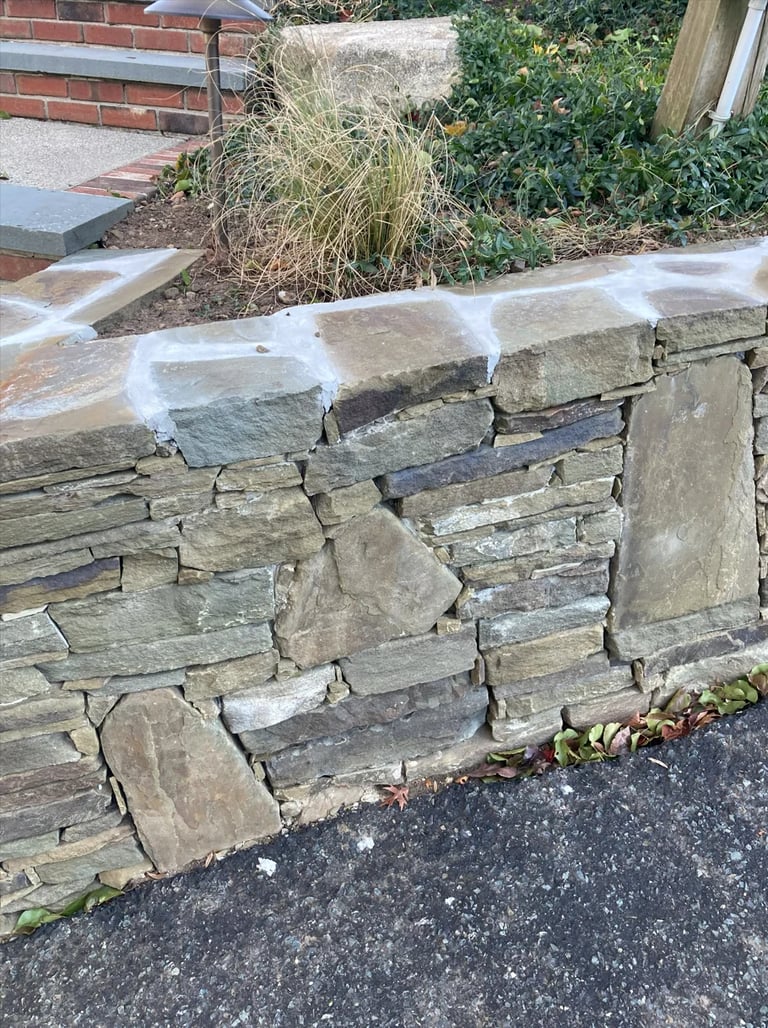 Weathered stone retaining wall with stacked slate blocks in a garden setting with dried grass and ivy in background