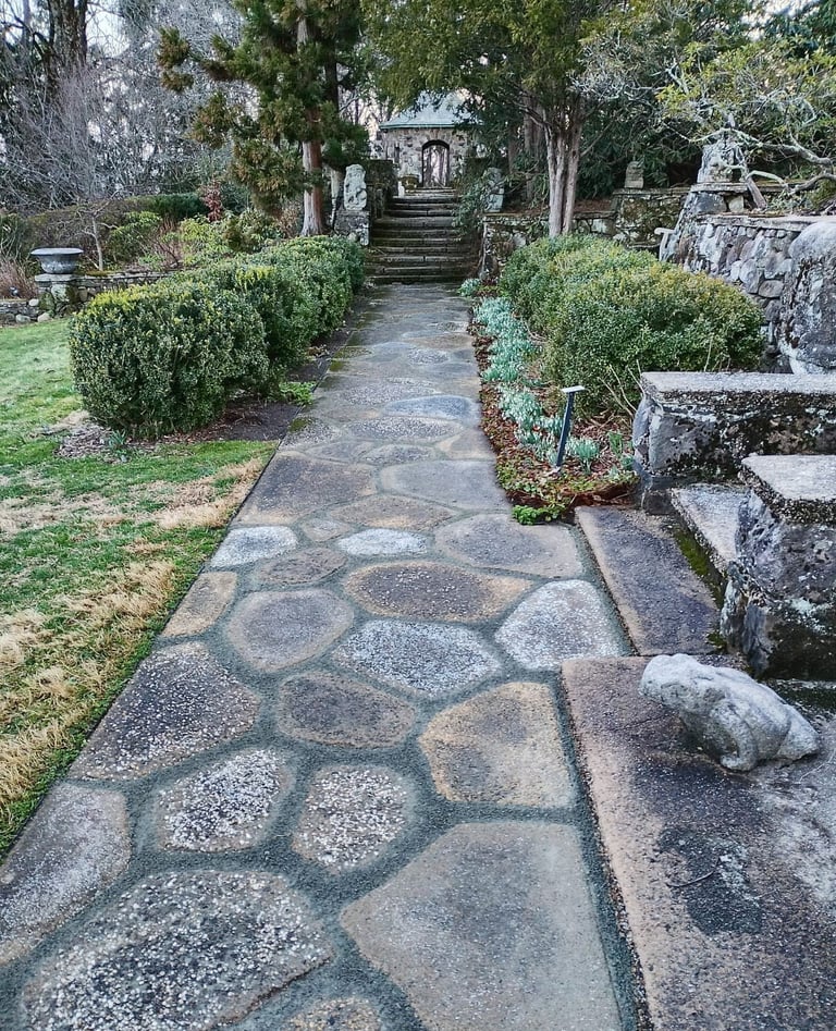 Stone pathway with circular pattern through gardens lined with hedges and large trees