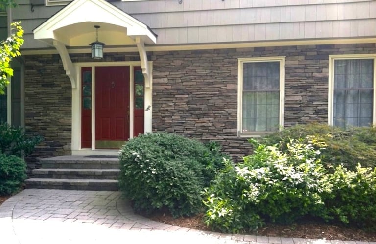 Modern brick home with red front door, white trim, and landscaped shrubs leading to the entrance