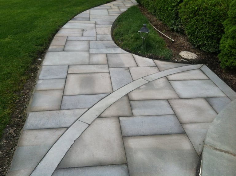 Curved stone patio pathway through green lawn with manicured hedges on the sides
