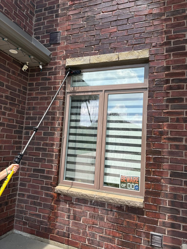 Person using water pole to clean window on brick building exterior with beware of dog sign