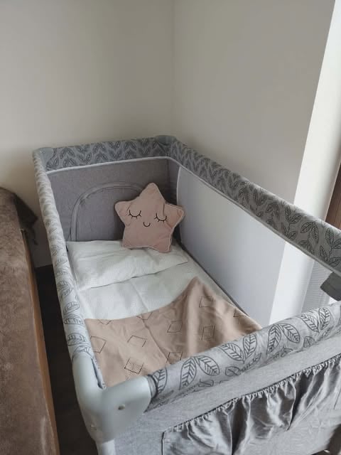 Gray and white baby bassinet with star-shaped pillow, bedding, and circular headrest in corner of white room
