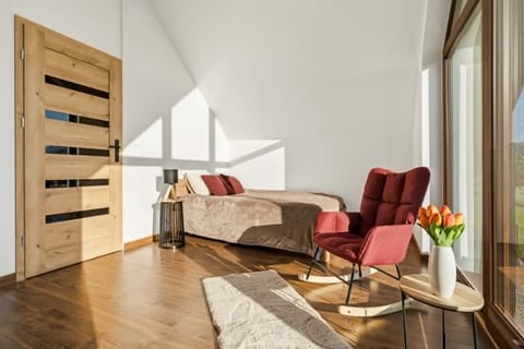 Modern loft bedroom with wooden floor, bed, burgundy armchair, large windows, and angled ceiling with skylights