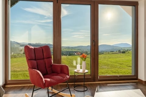 Red armchair and side table with flowers beside large windows overlooking rolling green hills and mountains