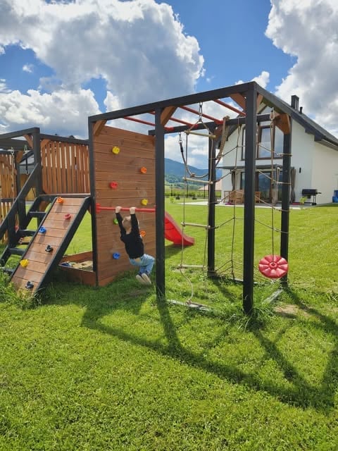 Child on wooden climbing structure with colorful features in grassy backyard with mountains in background