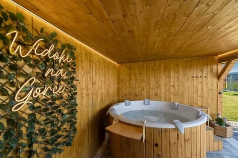 Interior of wooden hot tub shelter with neon welcome sign, round heated tub, and green climbing ivy on walls